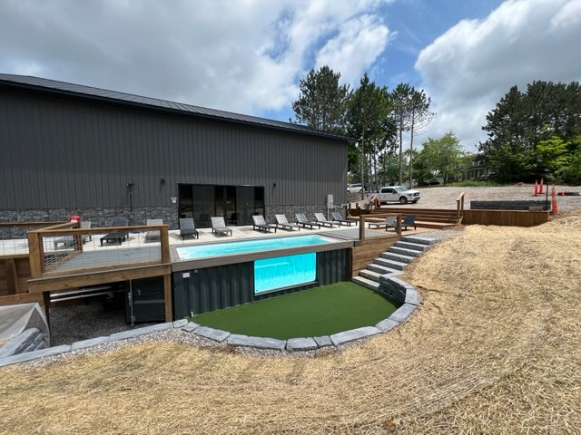 Container pool with viewing window set beside a pickleball barn with turf and decking